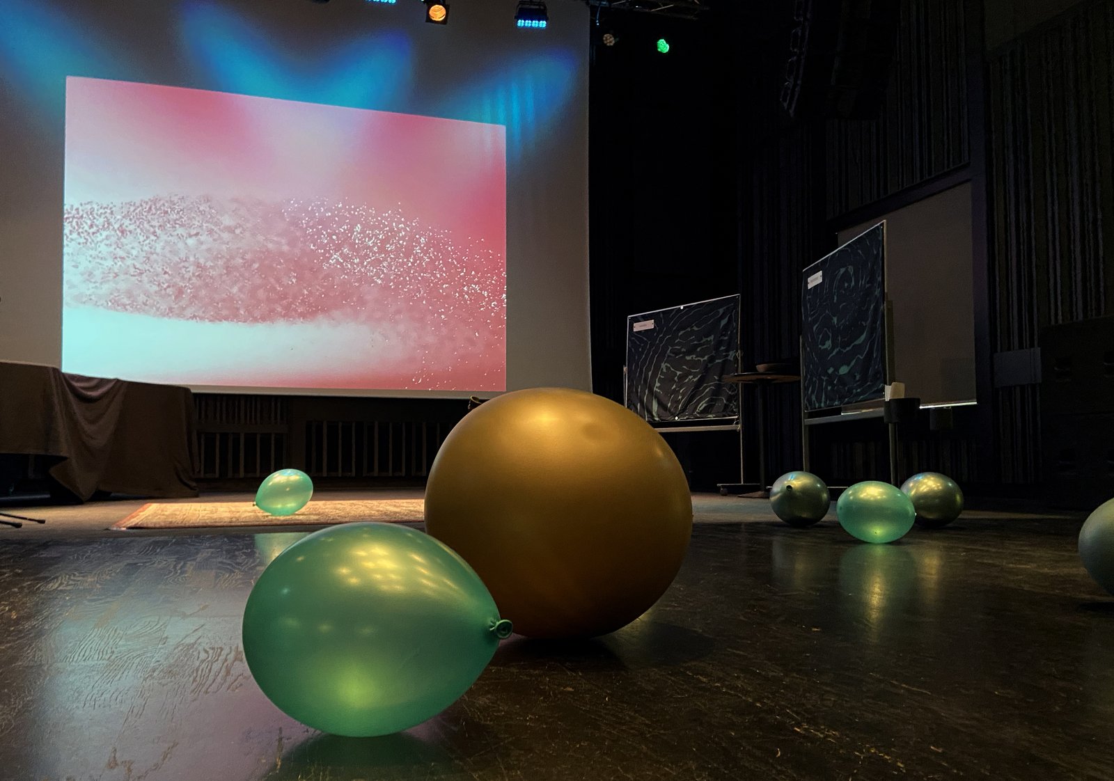 AMIS lab installation — pink projection on stage with gold and green balloons on the floor